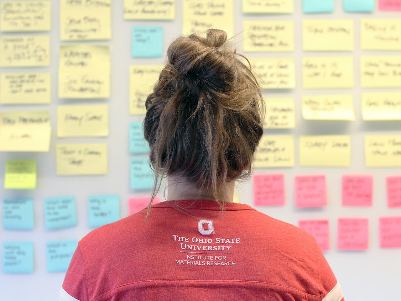 Female student wearing a red shirt looking at a board of notes