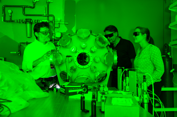 Profs. Enam Chowdhury, Wolfgang Windl and Lisa Hall inspect the "Death Star" vacuum chamber in Chowdhury’s Femtosecond Dynamics Lab where the XGRAY Laser will recreate the space radiation environment from Low Earth Orbit. The green glow comes from the system’s high-power pump lasers.