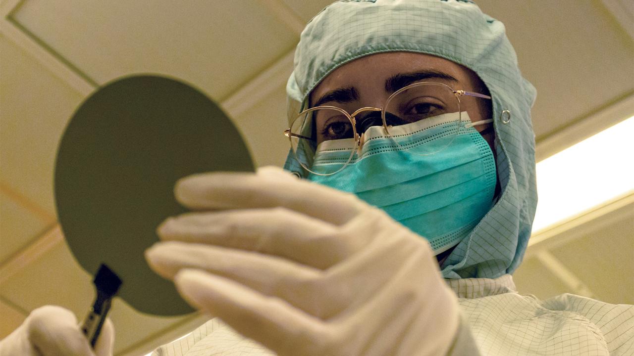 Person in PPE suit examining round piece of technology