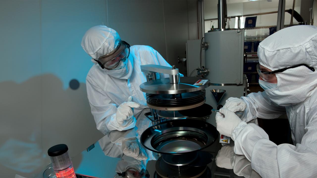 Two scientists in white suits and goggles working together